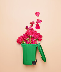 Flowers falling in trash container on orange pastel background