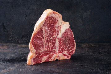 Raw dry aged wagyu porterhouse beef steak offered as close-up on rustic old board