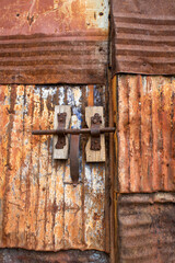 door made of rusted sheet steel plates, with a closed latch in its central part, corrosion, vertical