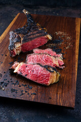 Modern style barbecue dry aged Chianina tomahawk steak sliced and served as close-up on a wooden...