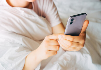 A close-up of a woman's hands holding a smartphone, a woman woke up lying in bed and started the day with an online viewing of a website.
