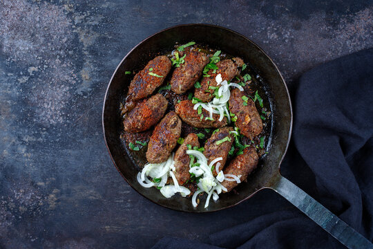 Traditional Croatian cevapcici spicy meat ball rolls with parsley and onion served as top view in a skillet with copy space