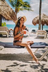 Mujer posando en bikini con un cóctel en una playa tropical
