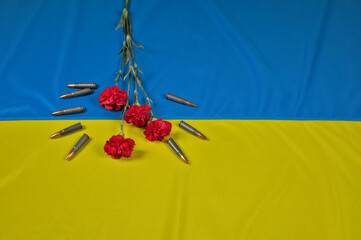 Red flower (surrounded by ammunition for Kalashnikov rifle) lying on a Ukrainian flag