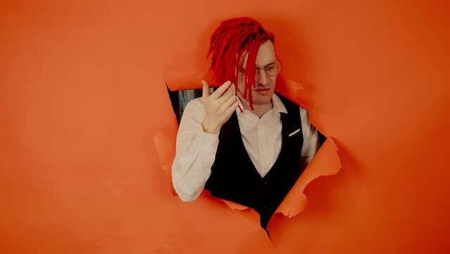 Well dressed man with bright hairstyle and thoughtful look sticking out of hole of orange background. Forgetful male in eyeglasses scratching head, trying to remember something.