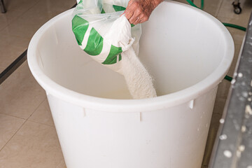 older man's hands pouring salt into plastic container to prepare brine