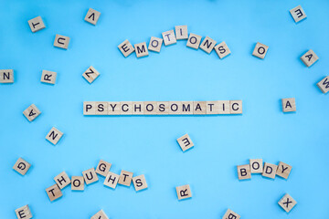 Words Psychosomatic, Emotions, Thoughts and Body on wooden blocks with letters on blue background. Minimal concept, top view
