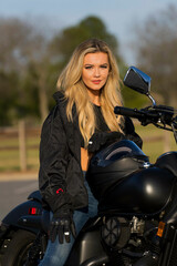 Obraz na płótnie Canvas A Lovely Blonde Model Enjoys The Outdoor Weather While Posing With Her Motorcycle