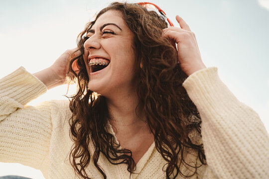 Happy girl with broad smile showing a tooth brace - Gen z woman wearing  red wireless headphones outdoors