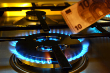 Close up of a lit gas cooker stove with a ten euro banknote in the background.