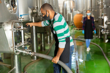 Working process at winery, man worker in protective mask working with fermentation tank