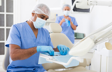 Obraz premium Focused hispanic dentist preparing to receive patient in dental office, checking and arranging tools
