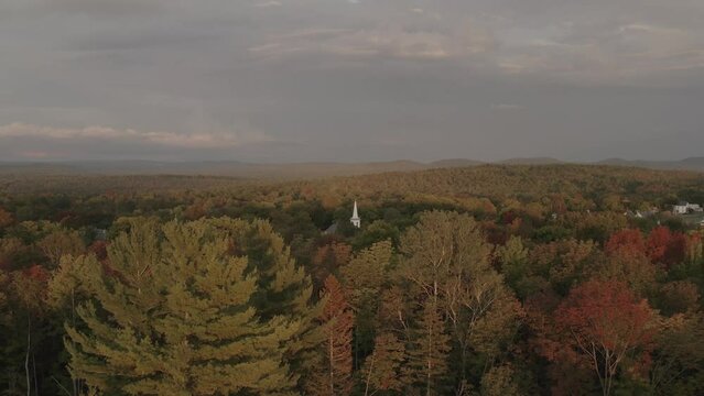 Church peaking above dense Fall colored woodland landscape aerial 