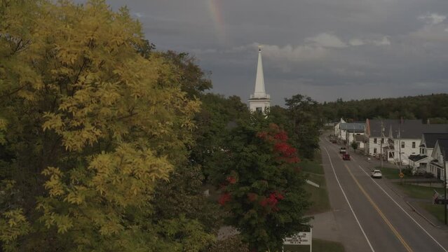 Aerial shot ascending roadside Monson Town revealing rainbow beyond church