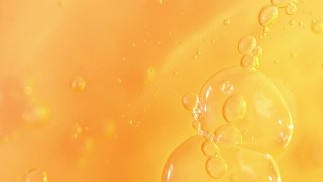 Vitamin C serum texture with dropper and slowly moving bubbles, orange cosmetics gel, macro shot.