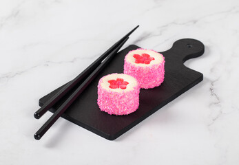 Mousse dessert. Sweet round sushi with pink jelly flower, sprinkled with coconut shavings on a serving board. Light background