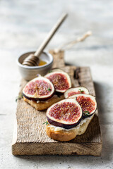 Two sandwiches with figs, thyme on a wooden board on textured background