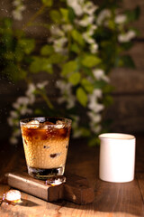 Iced coffee with cream on the table on a wooden board, flowers in the background, close-up
