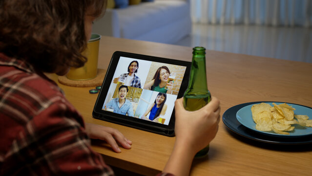Young happy attractive asia female enjoy relax night party event online celebration festive with friends at home sofa pr table clinking beer with glass and bottle drinking via online videocall.
