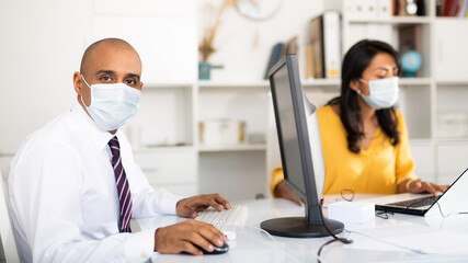 Director and secretary in protective medical masks work in the office