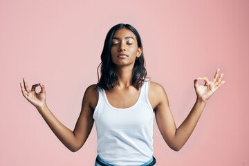 Namaste. Studio shot of a beautiful young woman meditating against a pink background.