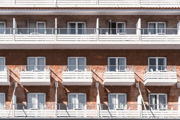 An exterior of a brick building with whiteboard balconies and glass doors. A resort hotel facade...