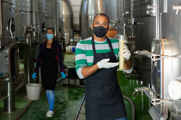 Man worker of winery in protective mask checking wine production process at fermentation tank
