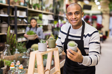 Positive man holding a potteds with cactuses in flower shop