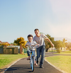 No training wheels needed. Shot of a father teaching his little son how to ride a bicycle in the...