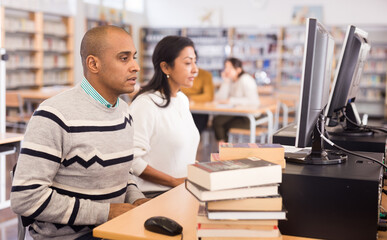 Interested latin american man studying in computer class in public library..