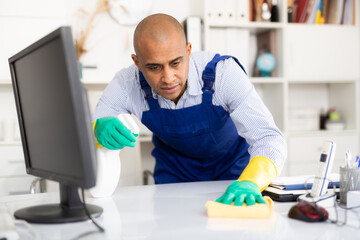 Man in an overalls cleans the table at office