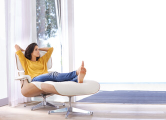 Appreciating the peace and quiet. An attractive woman relaxing on a chair with her hands behind her head.
