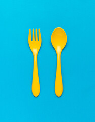 Bright yellow plastic spoon and fork on a blue background. Flat lay.