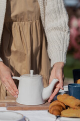 Women's hands hold a white teapot