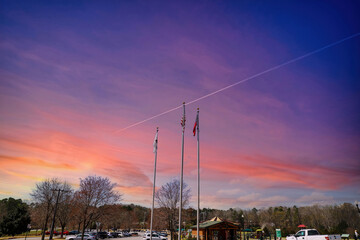 a stunning share of an American flag and two other flags flying on tall flag poles with parked cars, lush green trees with purple sky at sunset at Swift Cantrell Park in Kennesaw Georgia USA