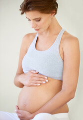 Great expectations. A beautiful young pregnant woman looking down at her bare tummy.