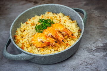Rice with shrimps in a frying pan on a wooden table.