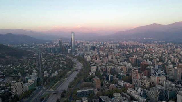Aerial dolly out of Met Park, Santa Maria towers and Mapocho river with Santiago skyline and hills in background at sunset, Chile