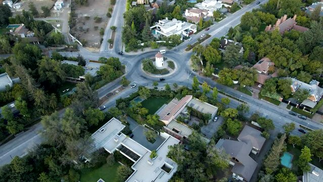 Aerial dolly out rising over Leonidas Montes windmill in roundabout with cars driving surrounded by trees, Lo Barnechea, Santiago, Chile