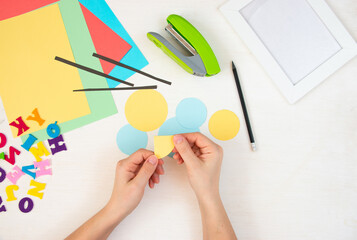 Women's hands fold multi-colored paper circles. Step by step instructions, top view. Step 9.