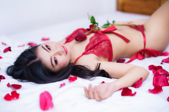 Tanned woman's body,Thailand Asian sexy young woman model in sexy red lingerie holding a red rose posing in bed with rose petals in the bedroom ,valentine's day concept