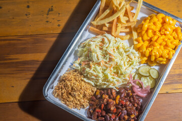American barbecue tray with several garnishes, among them, coleslaw salad, Mac n cheese, barbecue beans, and french fries.