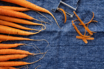 Carrots on a rustic blue linen towel with a metal carrot peeler  