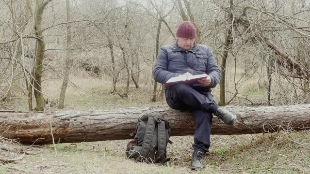 traveler thoughtfully reads a book in the forest sitting on a fallen tree