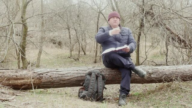 a tourist reads the Orthodox bible in the forest sitting on a fallen pine tree