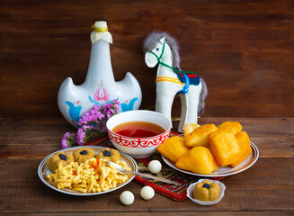Kazakh still life on Nauryz, with national food: baursaks, zhent, kurt, chak chak and tea on a wooden background