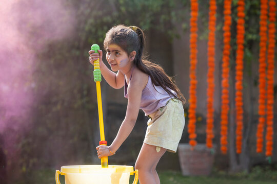 Little girl child celebrating Holi with pichkari and water colour