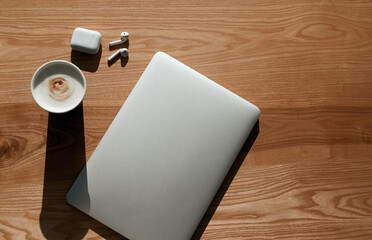 Laptop on wooden table with coffee and earbuds