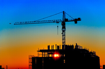 Die Silhouette des Rohbaus eines Gebäudes mit Baukran im Gegenlicht der untergehenden Abendsonne...