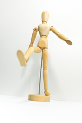 wooden mannequin holding up one leg, white background